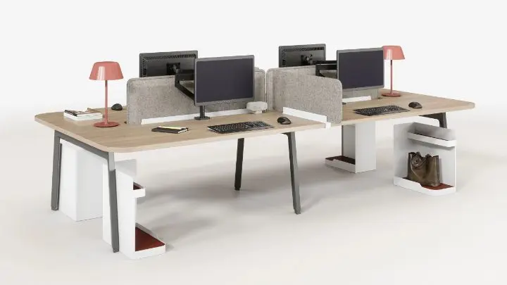 Four-person bench workstation on a white background with light-oak tops on grey A-legs, grey acoustic divider screens, monitor arms, coral task lamps and white under-desk storage with terracotta trays
